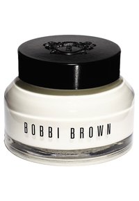 Produit crème blanc dans un pot en verre transparent avec un couvercle noir. L'étiquette indique "BOBBI BROWN" en lettres noires en gras. Forme arrondie, texture lisse.