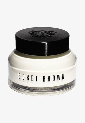 Biały krem w przezroczym szklanym słoiku z czarną nakrętką. Etykieta z napisem "BOBBI BROWN" dużymi czarnymi literami. Zaokrąglony kształt, gładka tekstura.