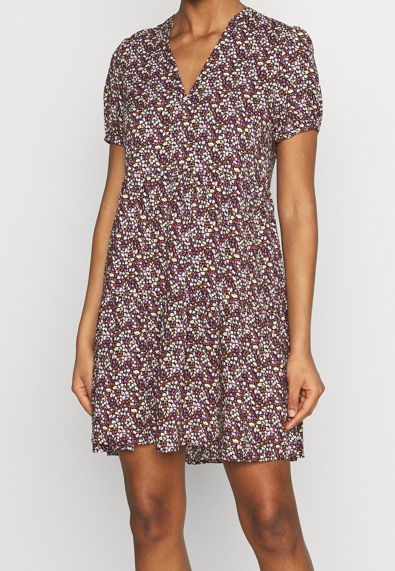 Blumenkleid mit V-Ausschnitt, kurzen Puffärmeln und lockerer Passform. Mit einem dunkelvioletten Hintergrund und kleinen, mehrfarbigen Blumenmustern.