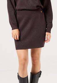 Strickrock in dunklem Burgunderrot mit glänzender Oberfl�äche, taillierter Passform und geripptem Bund. Akzentuiert mit einem kleinen Logodetail am Bund.