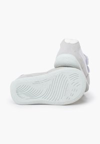 Suède en mesh schoenen met een lichtgrijze bovenkant, een witte gestructureerde hak en een geribbelde witte outsole met branding aan de zijkant.