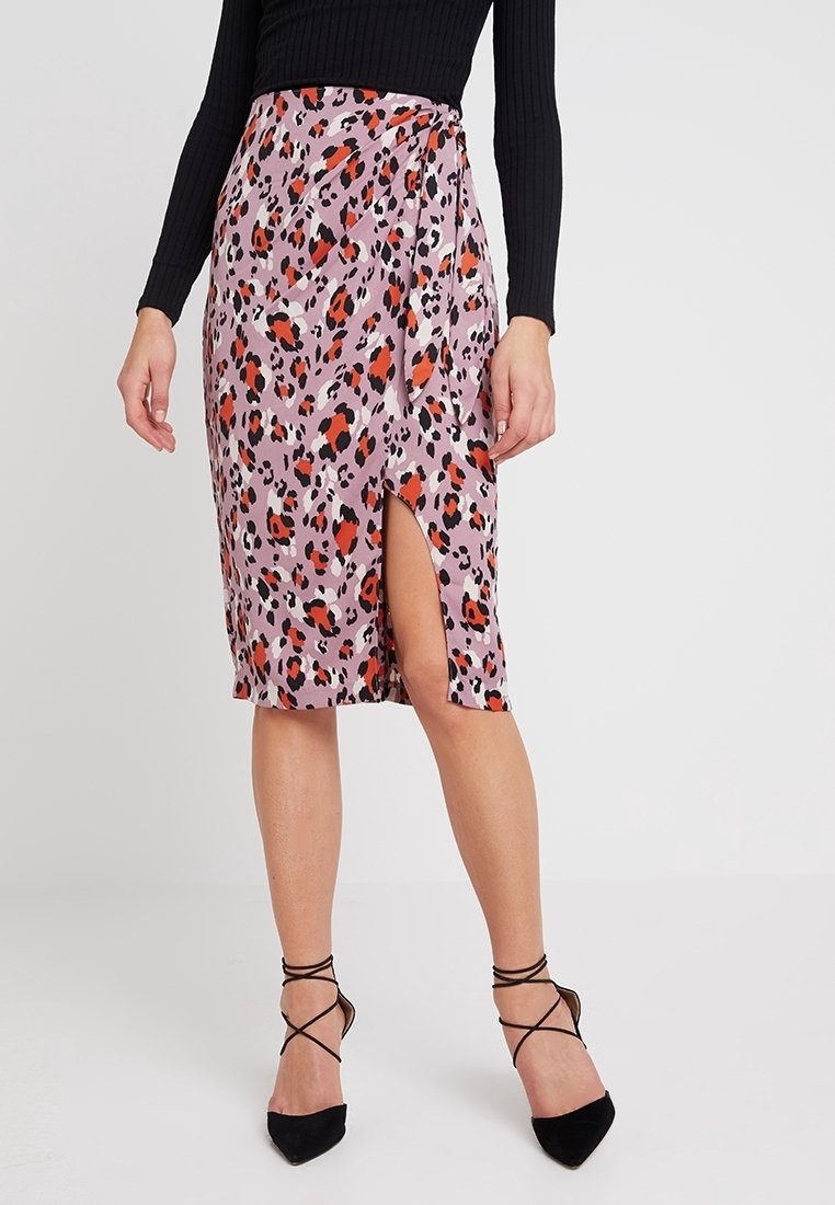 Falda con estampado de leopardo en rosa pastel, hecha de tela ligera, con una abertura lateral y detalle de lazo, combinada con tacones negros de tiras.