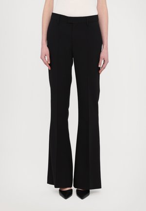Pantalons évasés noirs avec une texture lisse, devant plat et passants de ceinture. Caractéristiques d'une coupe ajustée, descendant jusqu'aux chevilles.