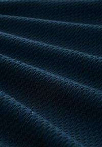 Tessuto blu scuro con un motivo ondulato e strutturato, caratterizzato da morbide pieghe che creano ombre e riflessi diagonali.