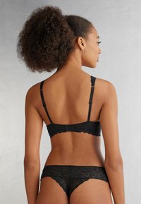Svart spets-bh med scallop-detaljer och justerbara axelband; matchas med svarta spets-trosor som har liknande scallop-detaljer.