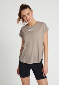 Beige t-shirt med kort ärm och rundad halsringning, med en vit logotyp på bröstet, tillsammans med svarta cykelshorts. Slät textur.