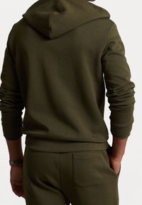 Olivgrön hoodie gjord av mjukt tyg, med huva, ribbade mudd och en avslappnad passform. Inkluderar en ficka på baksidan av matchande joggers.