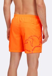 Pantaloni da bagno arancioni con una superficie liscia, caratterizzati da un design floreale in una tonalità più scura sulla gamba sinistra e una tasca posteriore.