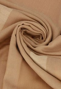 Tela beige, de textura suave, con un patrón tejido que presenta secciones más claras y más oscuras, enrollada ordenadamente para mostrar su forma estructural.