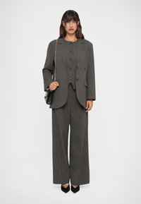 Completo grigio a righe con giacca doppiopetto dotata di grandi bottoni e pantaloni a gamba larga. Accentuato da una piccola borsa nera.