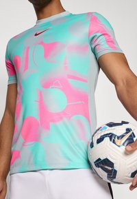 Nike träningströja med ett turkos och rosa abstrakt mönster, korta ärmar och rund halsringning. En vit och marinblå fotboll hålls.