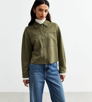 Olive green cropped jacket with a button-up front, two chest pockets, and a classic collar. Worn over a white turtleneck and blue jeans.
