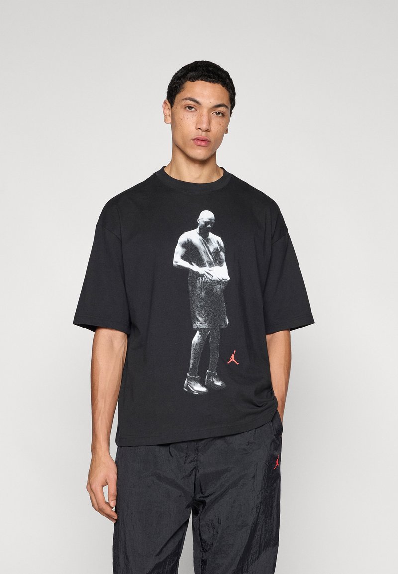 Μαύρο βαμβακερό t-shirt με στρογγυλή λαιμόκοψη, που διαθέτει άσπρο γραφικό με μια φιγούρα και μικρό κόκκινο λογότυπο Jordan στο κάτω μέρος. Χαλαρή εφαρμογή.