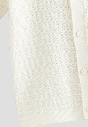 Hvid strikket cardigan med et tekstureret mønster, der har knapper foran samt ribstrikkede manchetter og kant. Blødt, letvægtsstof.