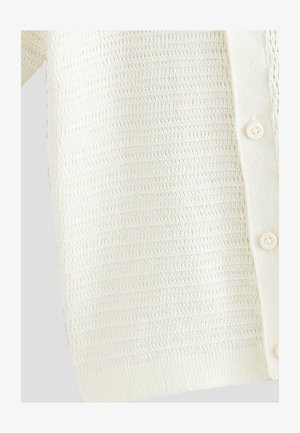 Valge heegeldatud kampsun tekstuurse mustriga, millel on ees nupud ning soonilised varrukaotsad ja alumine serv. Pehme, kerge kangas.