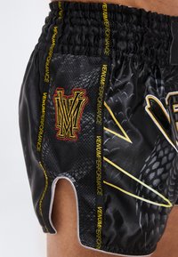 Μαύρο σορτς Venum Performance με κίτρινα στοιχεία, κόκκινο και κίτρινο κεντημένο λογότυπο και μια μικρή πλευρική σχισμή πάνω από τον μηρό.