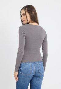 Long-sleeve grey top made of soft fabric, fitted design with a round neckline, paired with light blue denim jeans featuring back pockets.