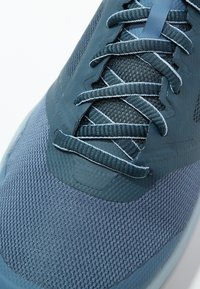 Blue athletic shoe featuring a mesh upper, textured lacing system, and rubber outsole. Includes contrasting accents in lighter tones.
