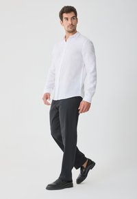 Hvid linned skjorte med lange ærmer og knap-ned krave, kombineret med sorte bukser og sorte sko; glat tekstur og klassisk pasform.