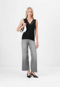 Black tank top with lace neckline, gray wide-leg jeans, and black pointed-toe heels. Carrying a small white handbag with black accents.