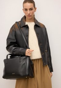 Czarna skórzana torebka o strukturalnym kształcie, z dwoma uchwytami u góry i paskiem na ramię; gładka tekstura z minimalną ilością detali metalowych.