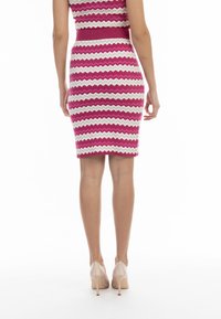 Rochie bodycon tricotată cu un model în zigzag roz și alb, design fără mâneci, talie strânsă și tiv până la genunchi. Asortată cu tocuri nude.