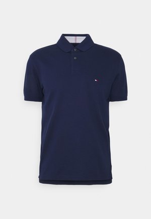 Polo bleu marine à manches courtes avec deux boutons et un petit logo rouge, blanc et bleu sur la poitrine gauche.