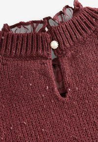 Pull en tricot bordeaux avec un col côtelé, présentant une ouverture en forme de clé et un bouton decoratif en perle ; texture douce avec de petites éraflures.