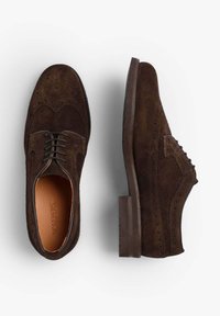 Zapatos de ante marrón con punta alada, con perforaciones decorativas, diseño de cordones, suela resistente y plantilla de cuero marrón suave.