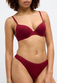 Μπράς μπορντό χωρίς καλώδια με ενισχυμένα cups και ρυθμιζόμεν�ους ιμάντες, σε συνδυασμό με μπικίνι χαμηλής μέσης με λογότυπο στον ζωνάρι. Απαλή υφή.