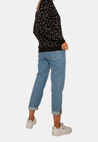 Felpa nera con stampa floreale bianca, abbinata a jeans di denim blu chiaro con risvolti e sneaker bianche con dettaglio del logo nero.