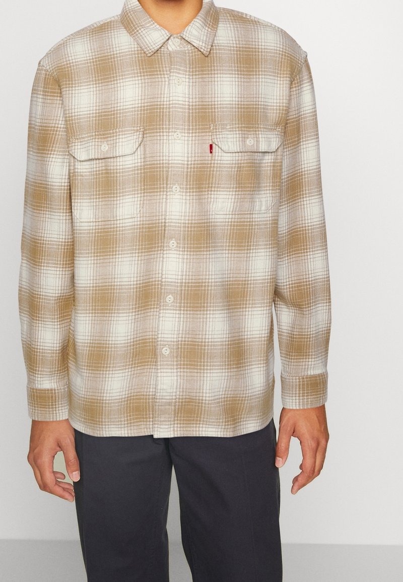 Camicia in flanella a quadri marroni e crema con design a bottoni, due tasche sul petto e maniche lunghe, realizzata in un materiale morbido al tatto.