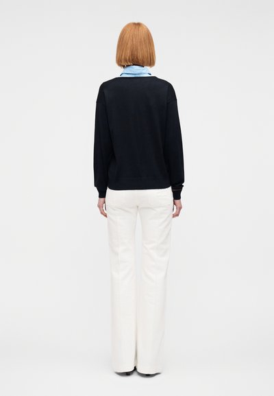 Μπλε σκούρο φούτερ με στρογγυλή λαιμόκοψη και μακριά μανίκια, συνδυασμένο με λευκό φαρδύ παντελόνι, εμφανιζόμενο από πίσω.