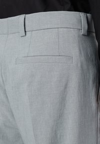 Lichtgrijze broek van een gladde, geweven stof. Beschikt over een platte achterzak en een getailleerde tailleband. Gedetailleerde stiksels langs de naden.