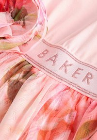 Rosa Miederkleid mit floralem Tüllüberzug, ausgestattet mit einem Band mit "BAKER" in silberner Stickerei, das zarte Texturen und Schichten präsentiert.