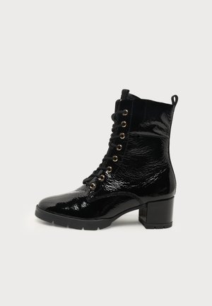 Bottine noire en cuir verni brillant avec lacets à l'avant et petit talon bloc sur un fond clair uni.