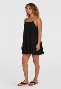 Robe sans manches noire avec un corsage cintré et un ourlet à volants en étages. Fabriquée en tissu léger, avec des bretelles fines et réglables.