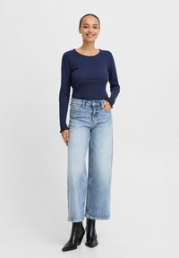 Marineblaue, gerippte Langarmbluse, kombiniert mit hellblauen, weit geschnittenen Jeans und schwarzen, knöchelhohen, schwindelfreien Stiefeln. Glatte Stoffe und entspannter Schnitt.