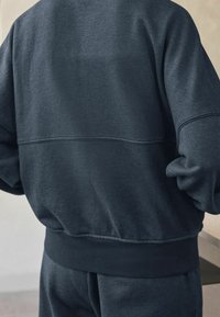 Donkerblauwe sweatshirt met ribgebreide manchetten en zoom, gemaakt van een textuurstof en met een eenvoudig, gestroomlijnd ontwerp. Het achteraanzicht toont contrasterende naaddetails.