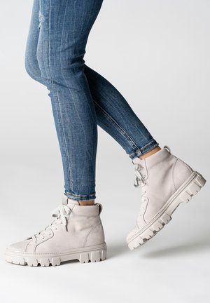 Baskets montantes en cuir gris clair avec lacets blancs, finition texturée et semelle épaisse. Portées avec un jean bleu ajusté.