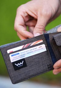 Folded wallet made of textured gray fabric, featuring card slots with visible identification cards, and a black logo patch with RFID symbol.