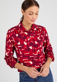 Camicia con motivo rosso e bianco, colletto, maniche lunghe, chiusura con bottoni e vestibilità rilassata. Il design presenta forme astratte.