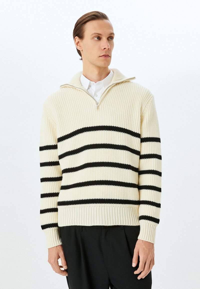 Cremefarbener, gestrickter Pullover mit schwarzen, horizontalen Streifen, Reißverschlusskragen, gerippten Bündchen und Saum. Strukturierter Stoff mit einer lockeren Passform.