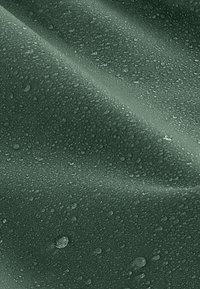 Tessuto impermeabile verde scuro con una texture liscia, caratterizzato da gocce d'acqua visibili sulla superficie, che evidenziano la sua qualità idrorepellente.