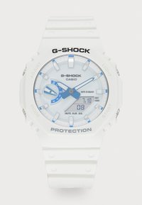 Montre G-SHOCK blanche avec un bracelet en résine, boîtier rond, accents bleus, écran numérique, étanche jusqu'à 20 bars et fonctionnalités ajustables.