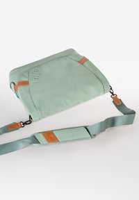 Borsa verde menta con una superficie liscia, dotata di dettagli in pelle marrone e una tracolla removibile. Chiusura con zip e design minimalista.