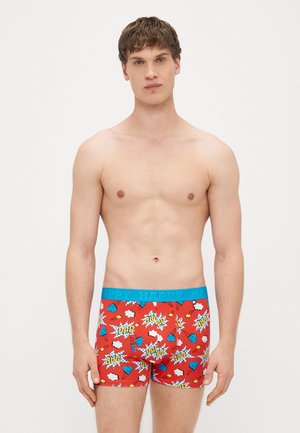 Sarkani bokseršorti ar zilu elastīgu jostu, rotāti ar krāsainiem komiksu stila attēliem, tostarp sirdīm un vārdu "TĒTIS".