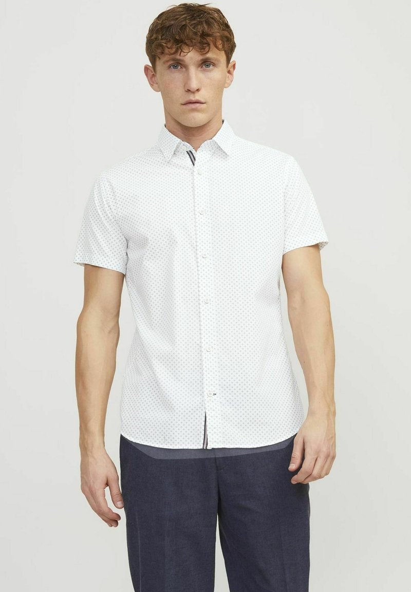 Camicia bianca a maniche corte, con un motivo a pois, realizzata in tessuto leggero. Presenta un colletto classico e una vestibilità dritta.