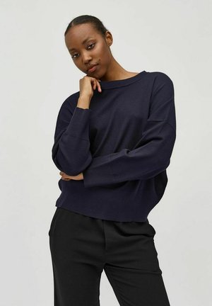 Navy knit sweater with a loose fit, wide boat neckline, and ribbed accents. Paired with black trousers, featuring a smooth fabric texture.
