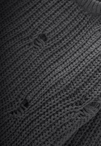 Tela de punto gris con un patrón texturizado; presenta varios agujeros y bordes deshilachados, mostrando un aspecto casual y desgastado.